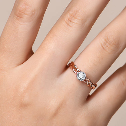 Gold ring with a braided band design and a round-cut clear central stone in a four-prong setting.

