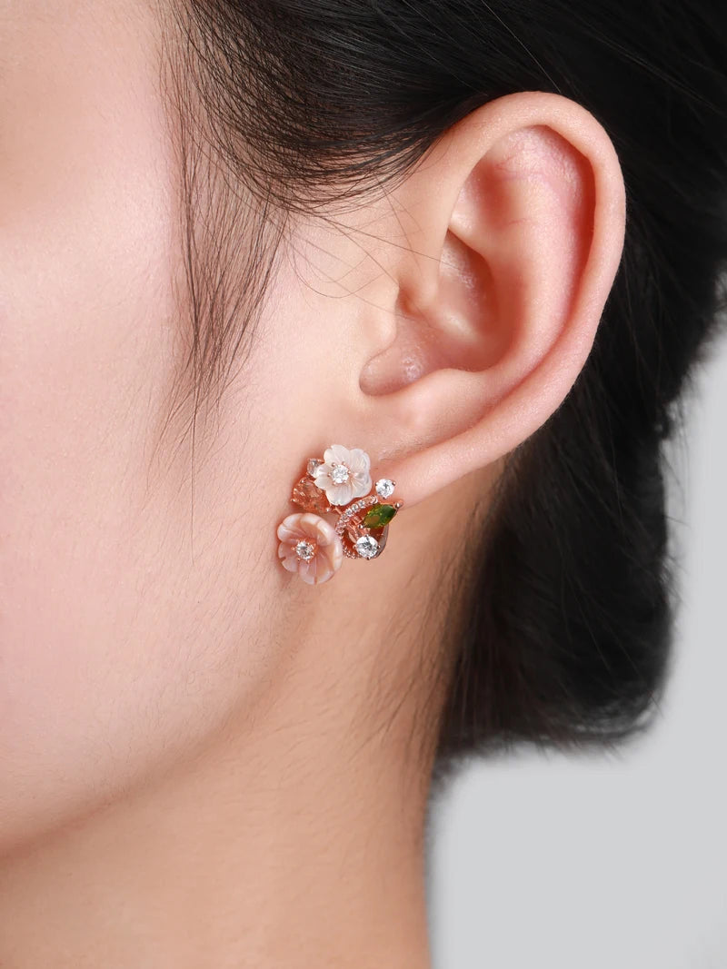 Begonia floral earrings with carved peach and ivory petals, accented by sparkling white and violet stones in a rose gold setting.

