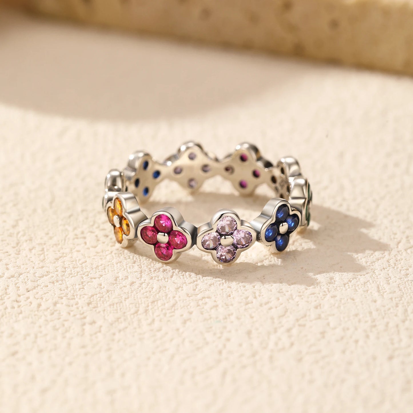 Silver ring with multicoloured four-petal flower gemstones set around the band.

