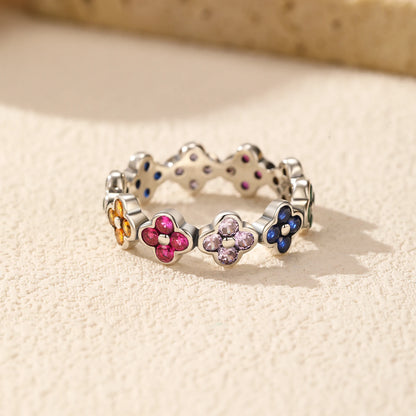 Silver ring with multicoloured four-petal flower gemstones set around the band.

