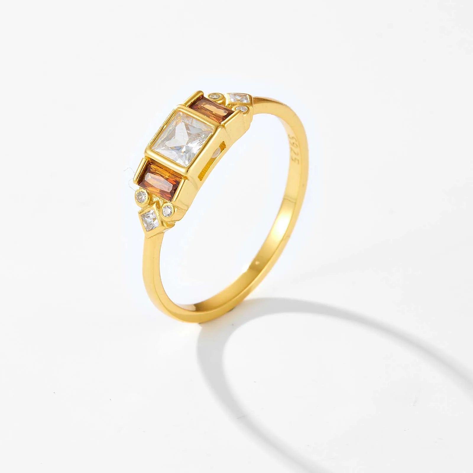 Gold ring with central white stone flanked by smoky square-cut stones and small accent gems


