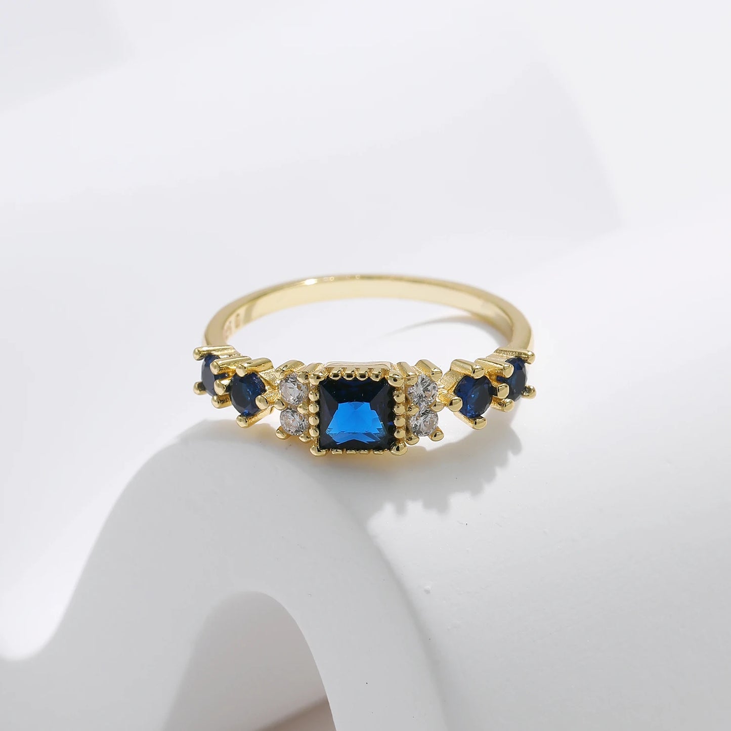 Gold-plated sterling silver ring with a central square-cut deep blue stone and surrounding clear round stones

