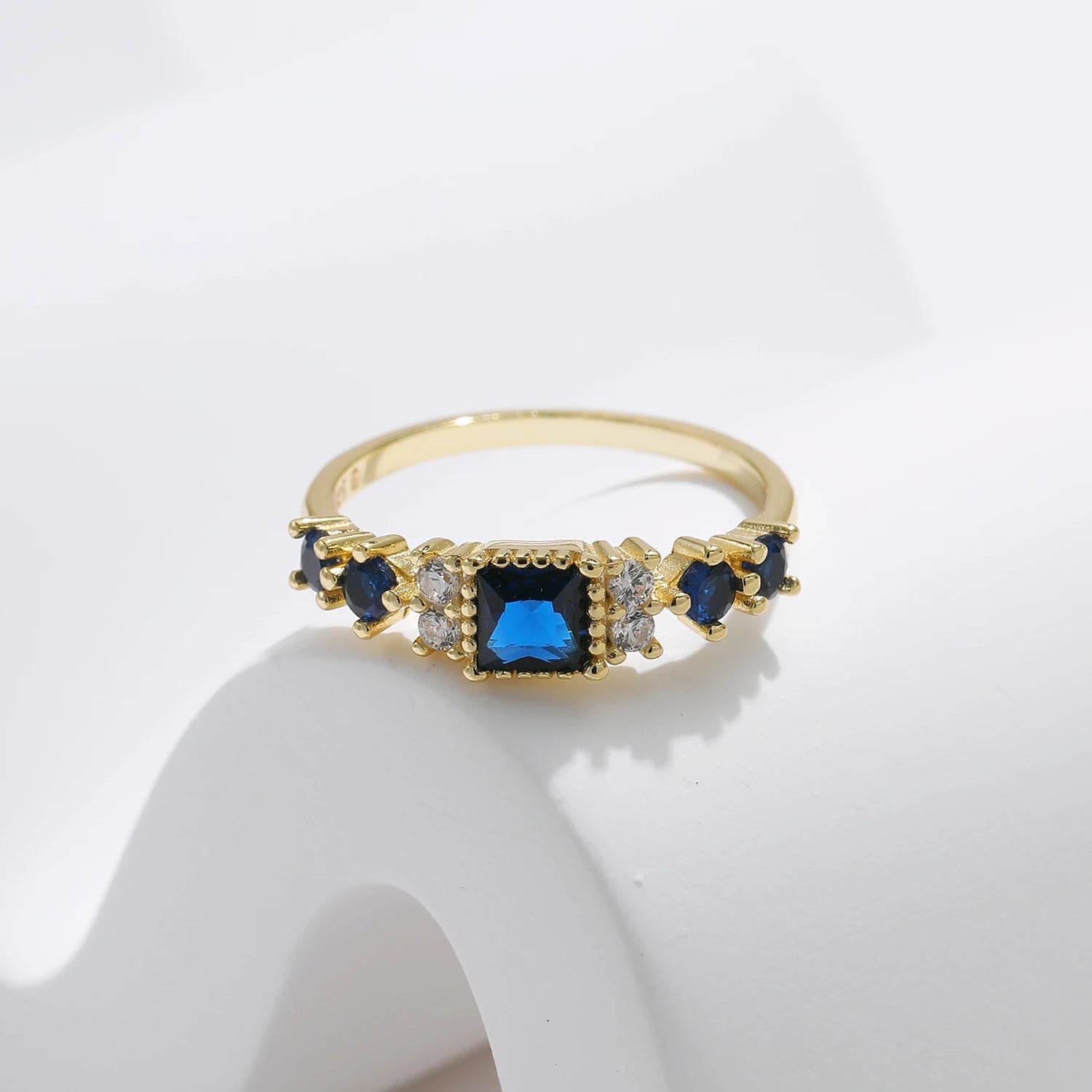 Gold-plated sterling silver ring with a central square-cut deep blue stone and surrounding clear round stones


