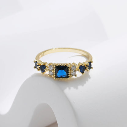 Gold-plated sterling silver ring with a central square-cut deep blue stone and surrounding clear round stones

