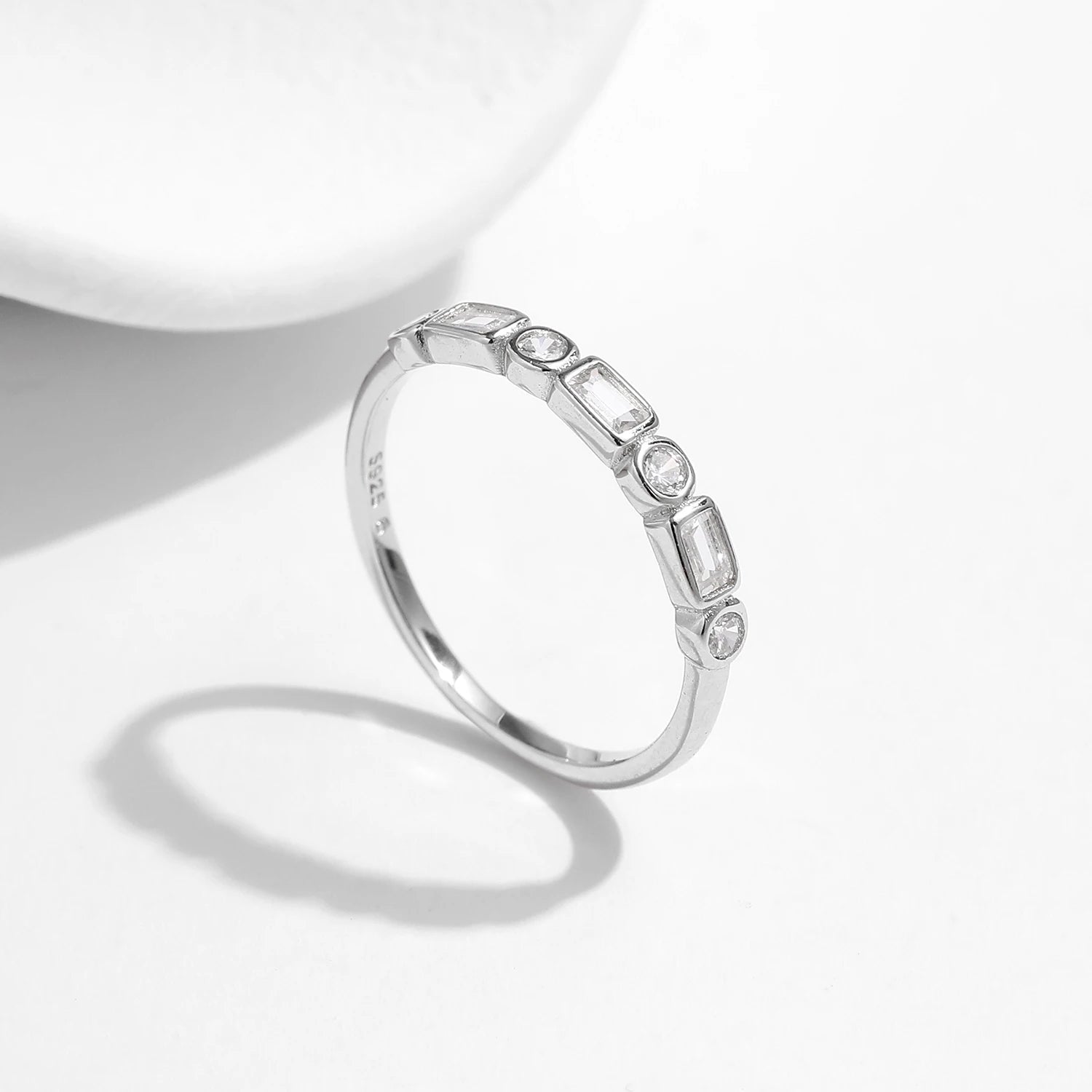 Silver ring featuring alternating round and baguette-cut white stones in a half-band setting.

