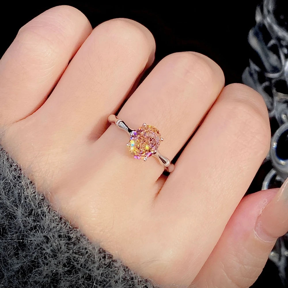 Silver band ring with an oval-cut pink-orange tourmaline stone, displayed against a deep red background from the Rossa collection.

