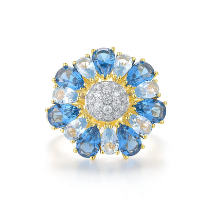 Gold ring shaped like a flower with alternating blue and clear pear-shaped stones around a pavé-set centre


