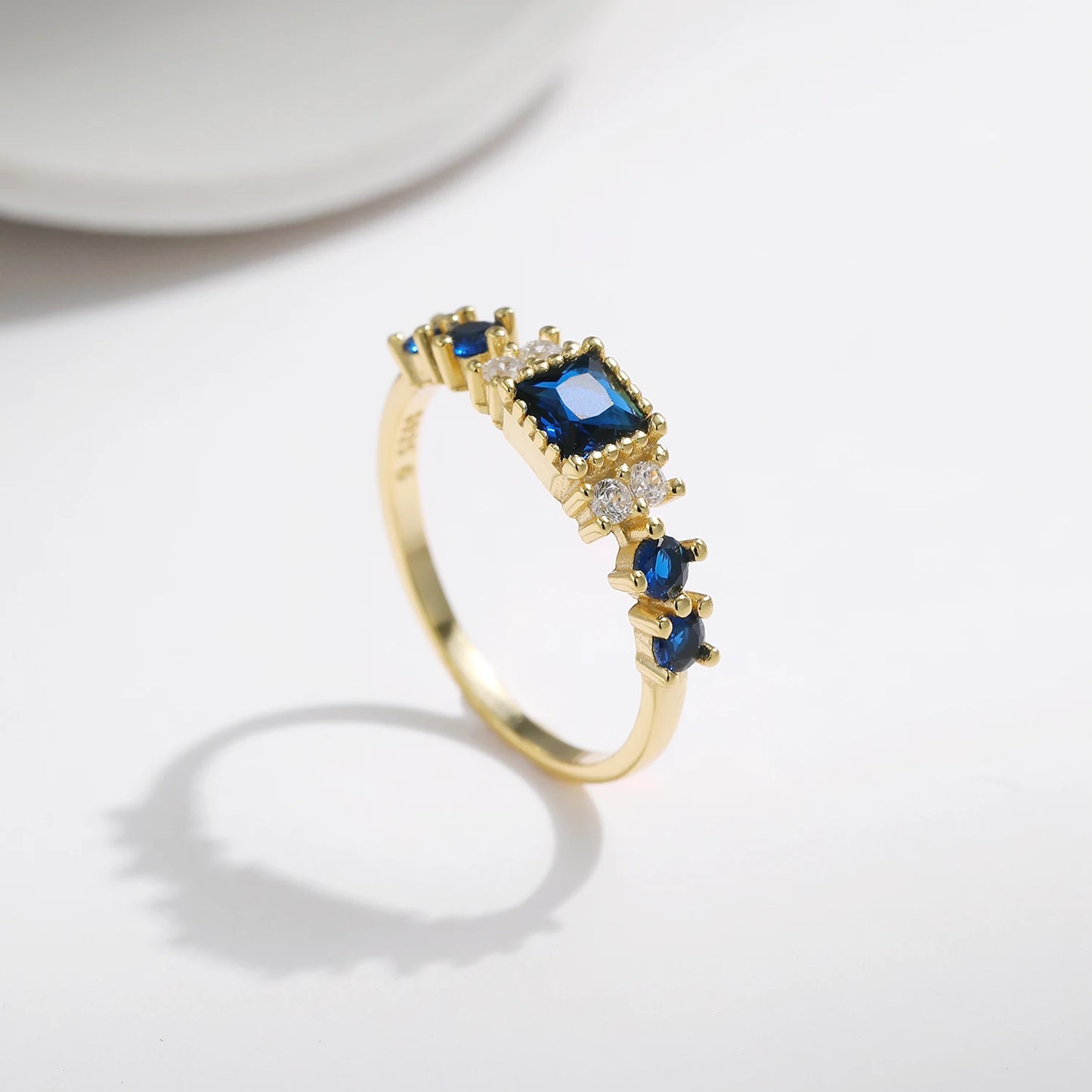 Gold-plated sterling silver ring with a central square-cut deep blue stone and surrounding clear round stones

