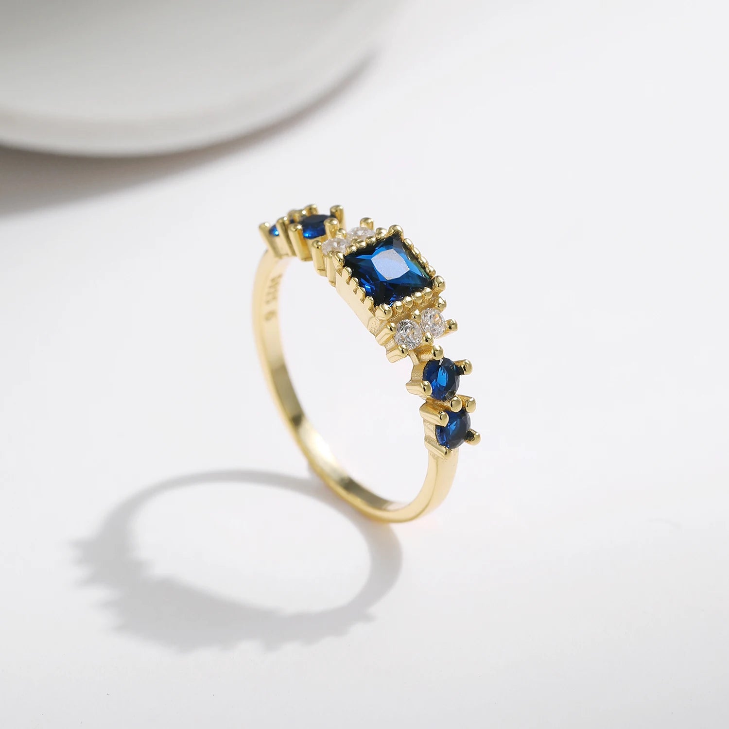 Gold-plated sterling silver ring with a central square-cut deep blue stone and surrounding clear round stones

