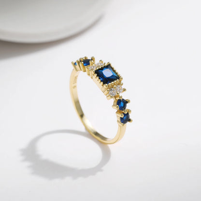 Gold-plated sterling silver ring with a central square-cut deep blue stone and surrounding clear round stones

