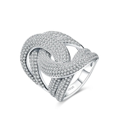 Wide silver ring with interlocking ribbon-like loops, entirely paved with sparkling white stones.

