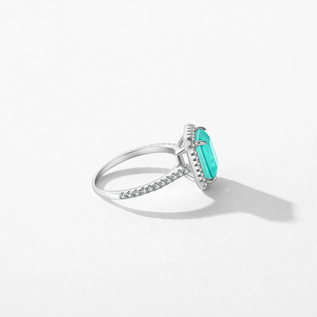 Rectangular green gemstone ring with a halo of clear stones on a silver band.


