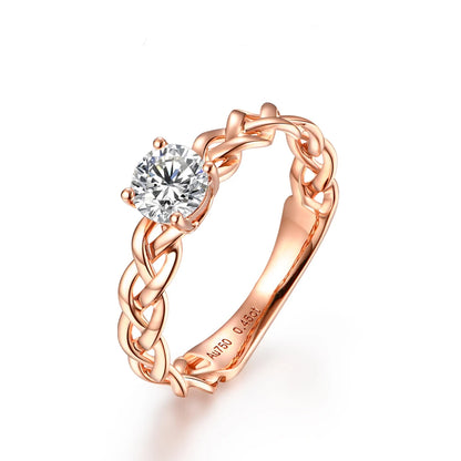 Gold ring with a braided band design and a round-cut clear central stone in a four-prong setting.

