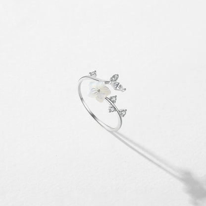 Delicate silver ring featuring a white carved flower and sparkling leaf-shaped stones arranged in a graceful, curved design.


