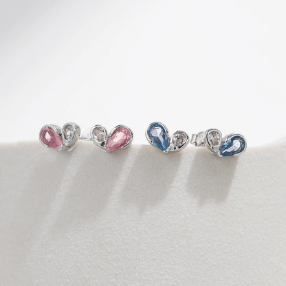 
Pair of silver earrings featuring a pink or blue heart-shaped gemstone paired with a smaller round clear stone in a modern open setting.



