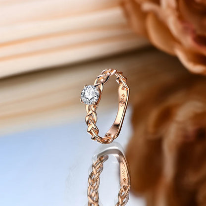 Gold ring with a braided band design and a round-cut clear central stone in a four-prong setting.

