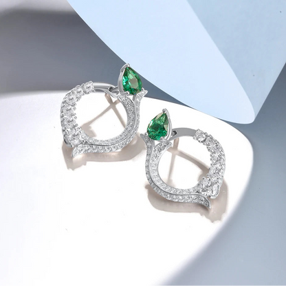 Silver earrings with circular diamond pave design and pear-shaped green jade stones at the top

