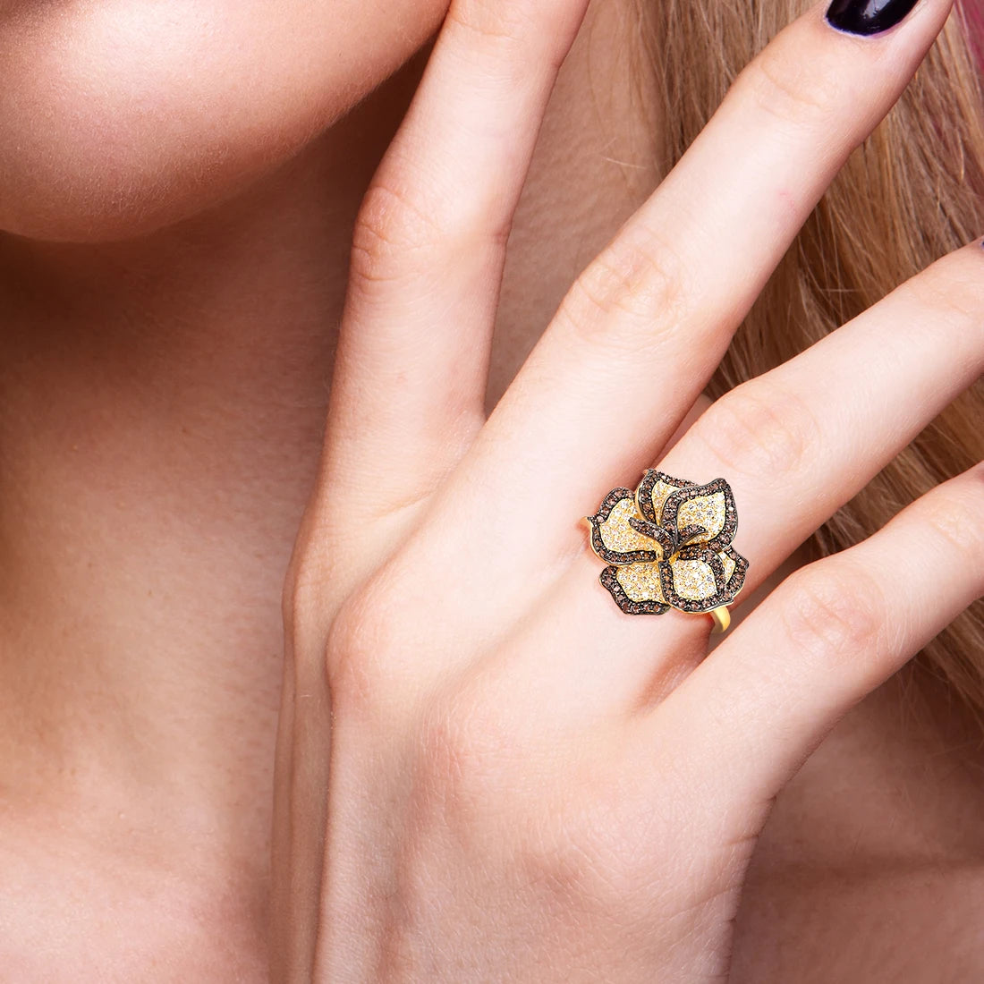 Gold ring with a large, sparkling flower design featuring white and brown stones on each petal.

