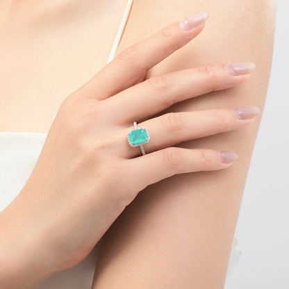Rectangular green gemstone ring with a halo of clear stones on a silver band.

