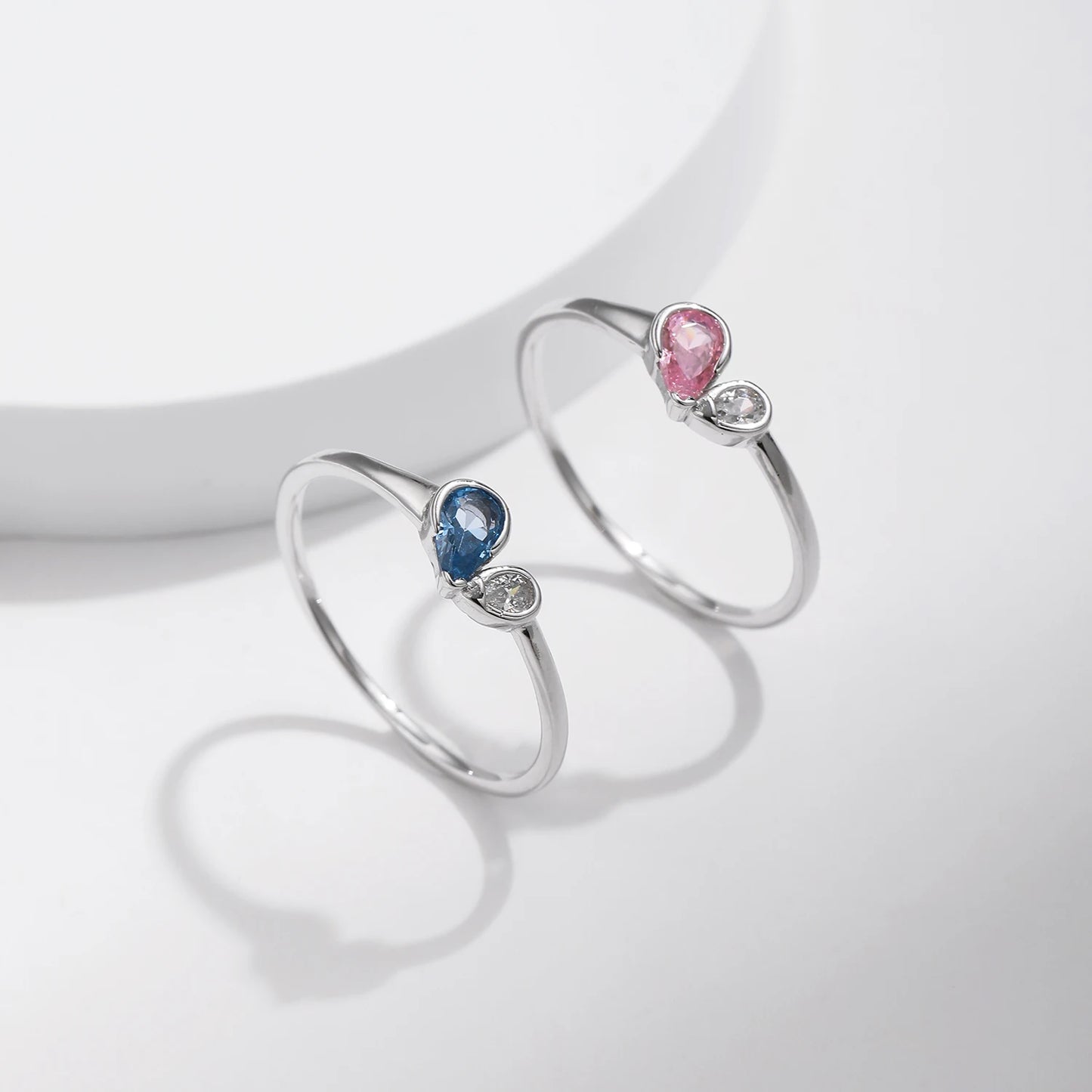 Sterling silver ring featuring a pink teardrop stone paired with a round clear stone in an open-heart inspired setting.

