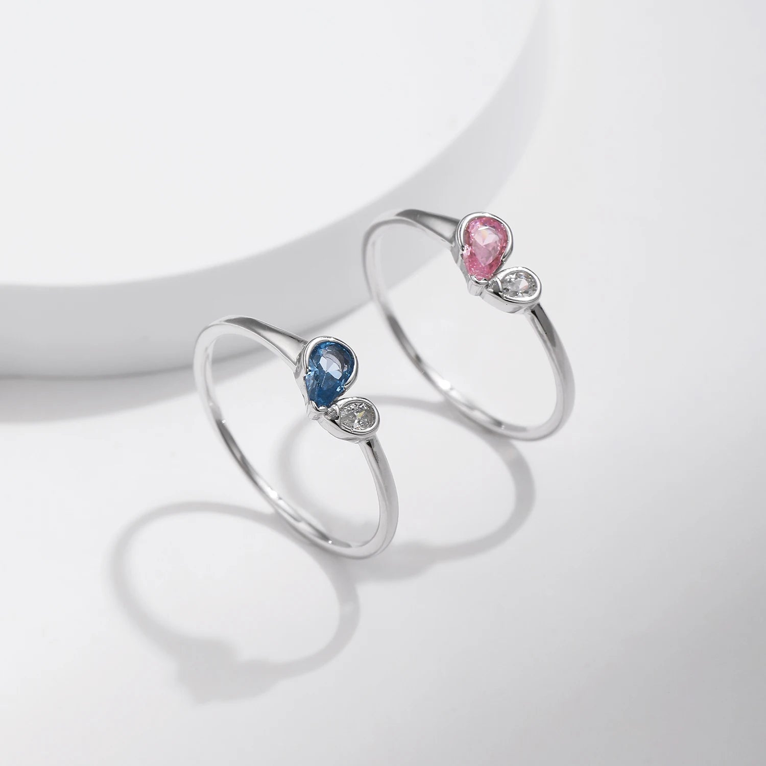 Sterling silver ring featuring a pink teardrop stone paired with a round clear stone in an open-heart inspired setting.

