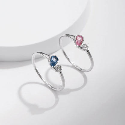 Sterling silver ring featuring a pink teardrop stone paired with a round clear stone in an open-heart inspired setting.


