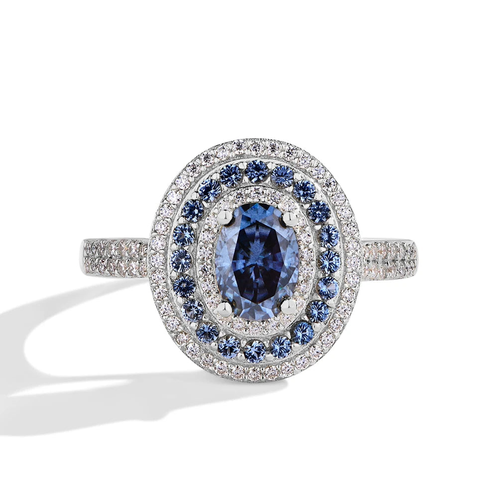 Sterling silver ring with an oval-cut deep blue gemstone surrounded by two concentric halos of white and blue stones, set on a pavé band
