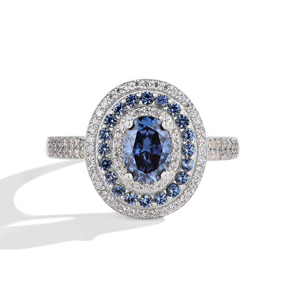 Sterling silver ring with an oval-cut deep blue gemstone surrounded by two concentric halos of white and blue stones, set on a pavé band