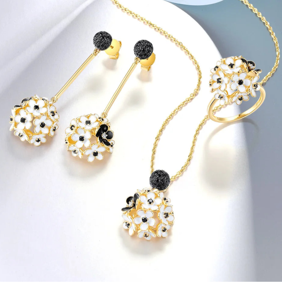 Fiore Scuro jewelry set featuring gold-tone earrings, ring, and pendant with white and black floral detailing from the Bianco Nero collection.

