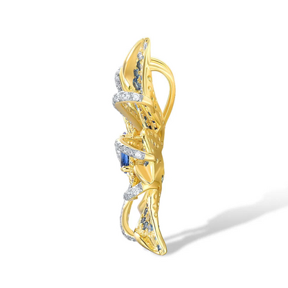 Gold floral brooch with layered petal-like curves, set with blue gemstones and clear pavé accents, featuring an oval sapphire-blue centerpiece