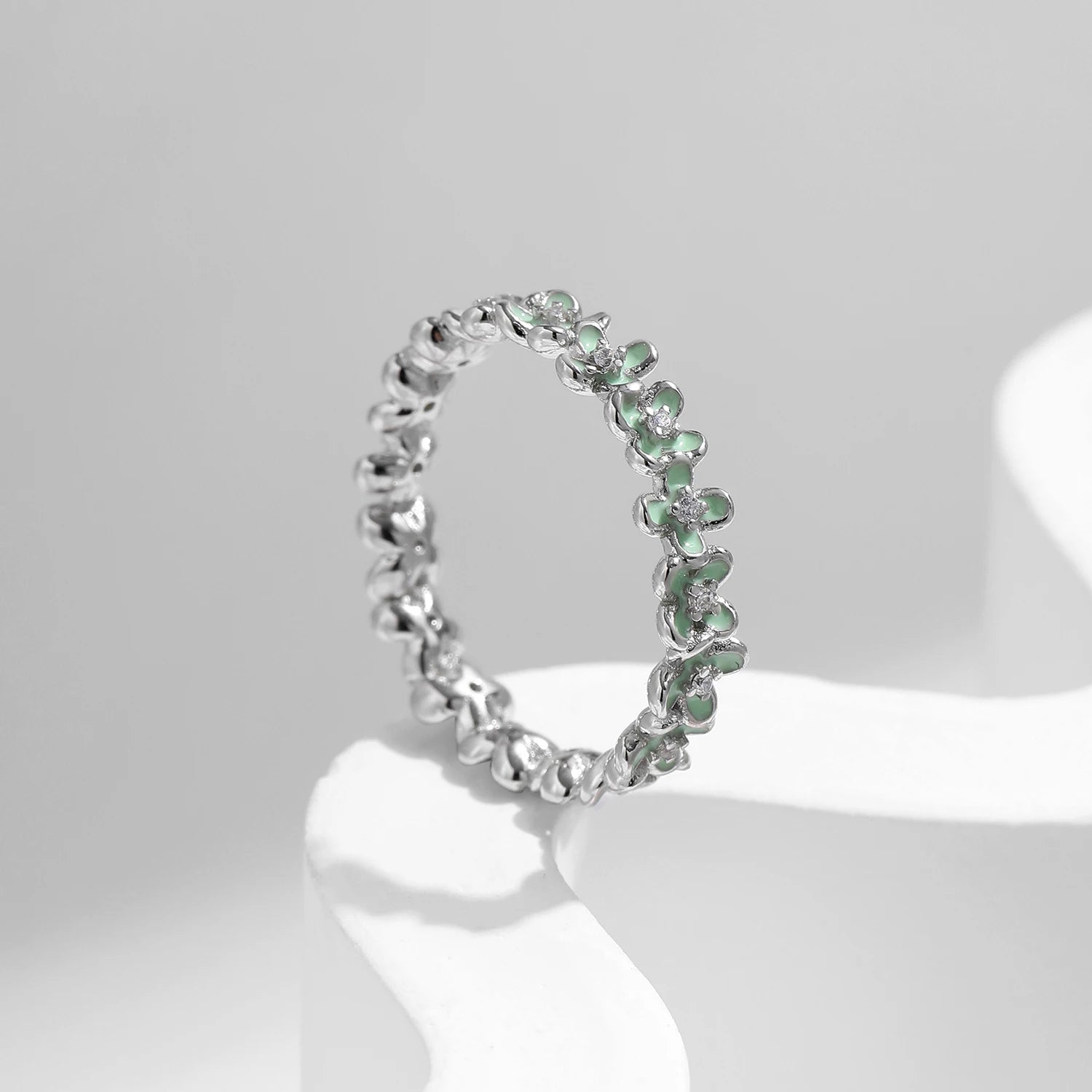 Sterling silver floral band ring with light green enamel petals and tiny diamond accents.

