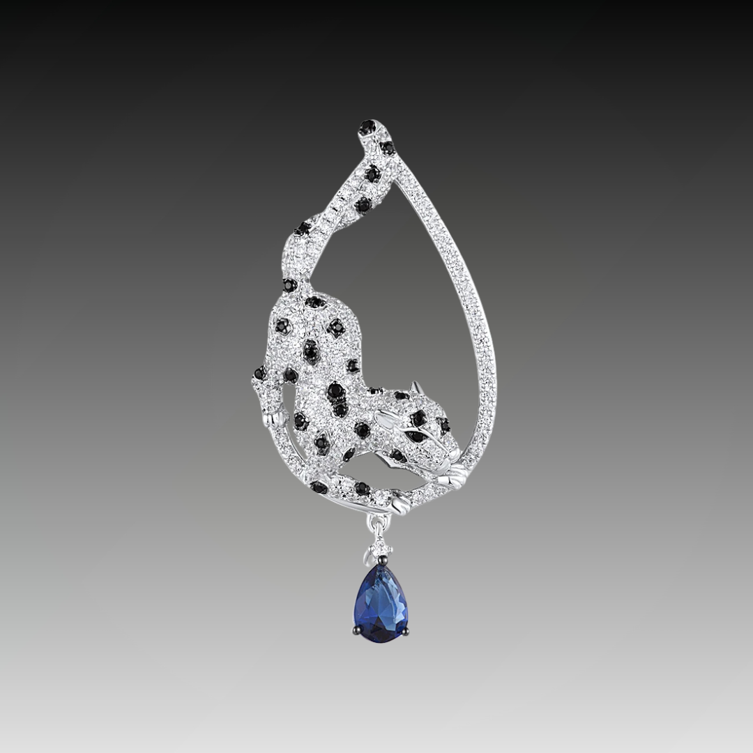 Leopard-shaped silver pendant with black stone spots, set within a teardrop frame and finished with a hanging blue teardrop gemstone.

