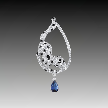 Leopard-shaped silver pendant with black stone spots, set within a teardrop frame and finished with a hanging blue teardrop gemstone.

