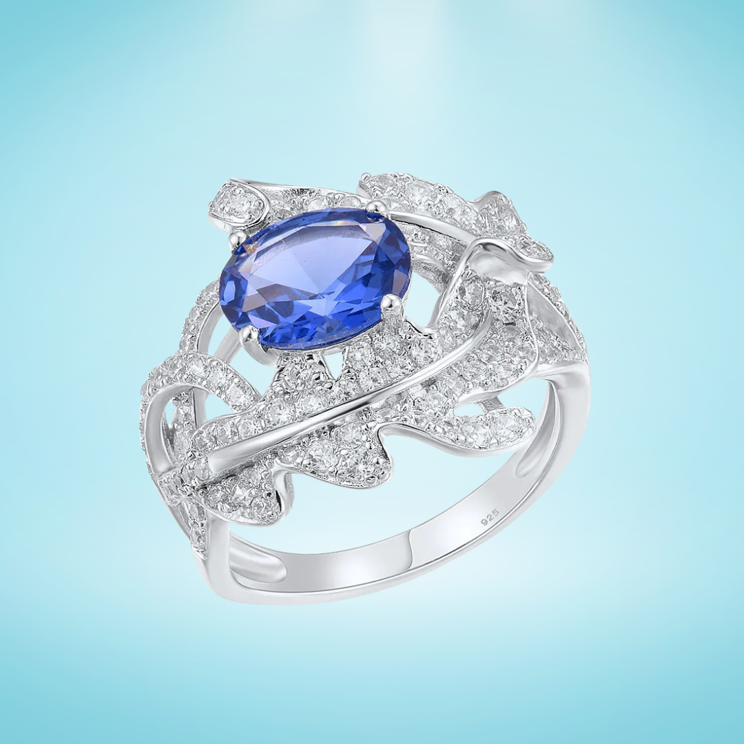 Silver ring with fern-like design, white pavé stones, and deep blue oval gemstone

