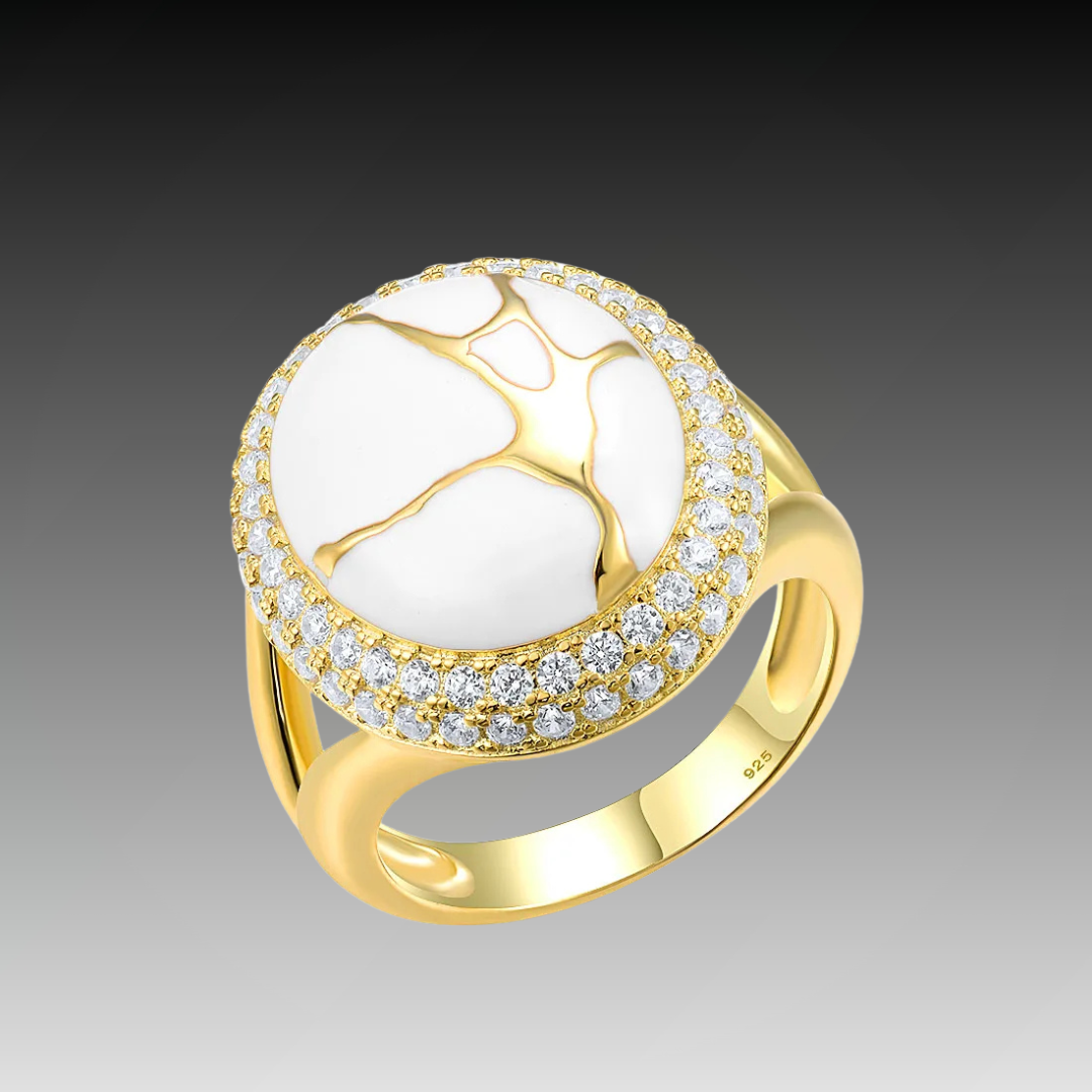 Gold ring with a large white stone featuring golden vein-like patterns, encircled by two rows of clear stones.

