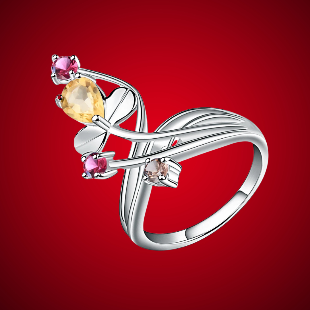 Silver ring with a flowing, branch-like design, featuring a pear-shaped yellow gemstone and smaller pink and light brown stones.

