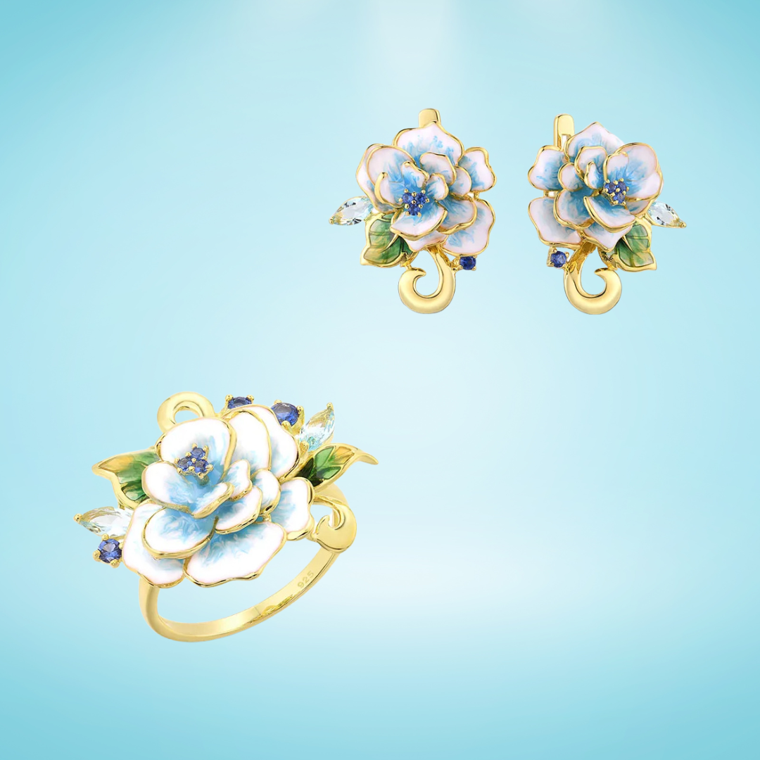 Gold-plated floral ring and matching earrings with white and light blue enamel petals, green leaves, and small blue accent stones.

