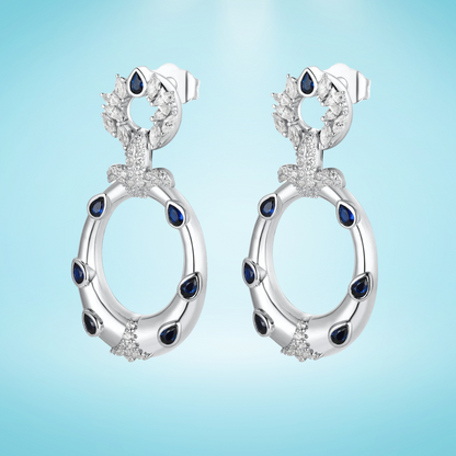 Sterling silver hoop earrings with blue teardrop stones and pavé crystal accents, inspired by underwater textures, displayed on a light blue background