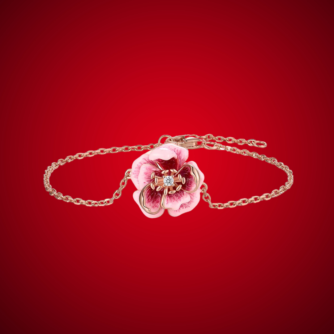 Anemone bracelet with a delicate chain and a central pink flower charm detailed with enamel and a sparkling center stone.

