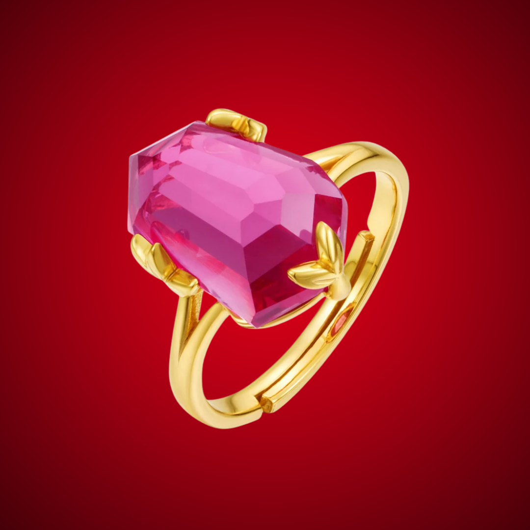 Gold ring with a bold, faceted pink gemstone held by petal-shaped prongs, displayed on a red background.


