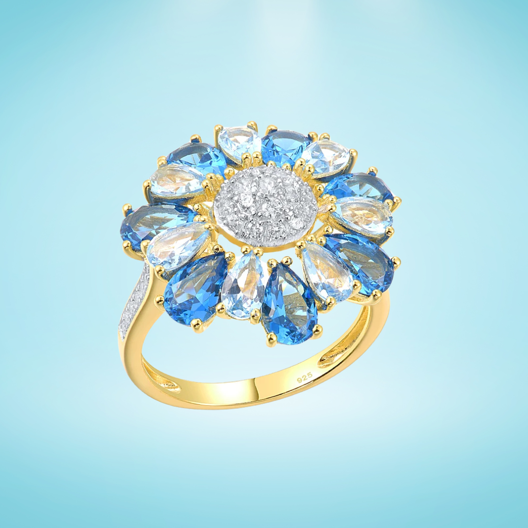Gold ring shaped like a flower with alternating blue and clear pear-shaped stones around a pavé-set centre

