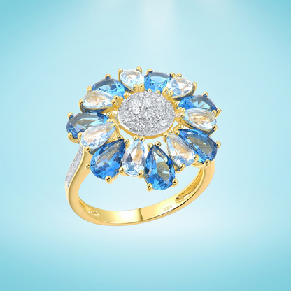 Gold ring shaped like a flower with alternating blue and clear pear-shaped stones around a pavé-set centre

