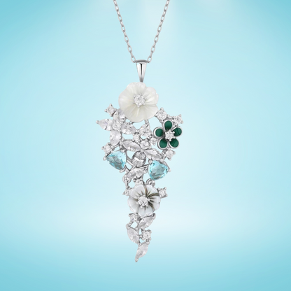 Pendant featuring carved mother-of-pearl flowers, green enamel petals, and aquamarine-blue stones set in silver with white zircon accents.

