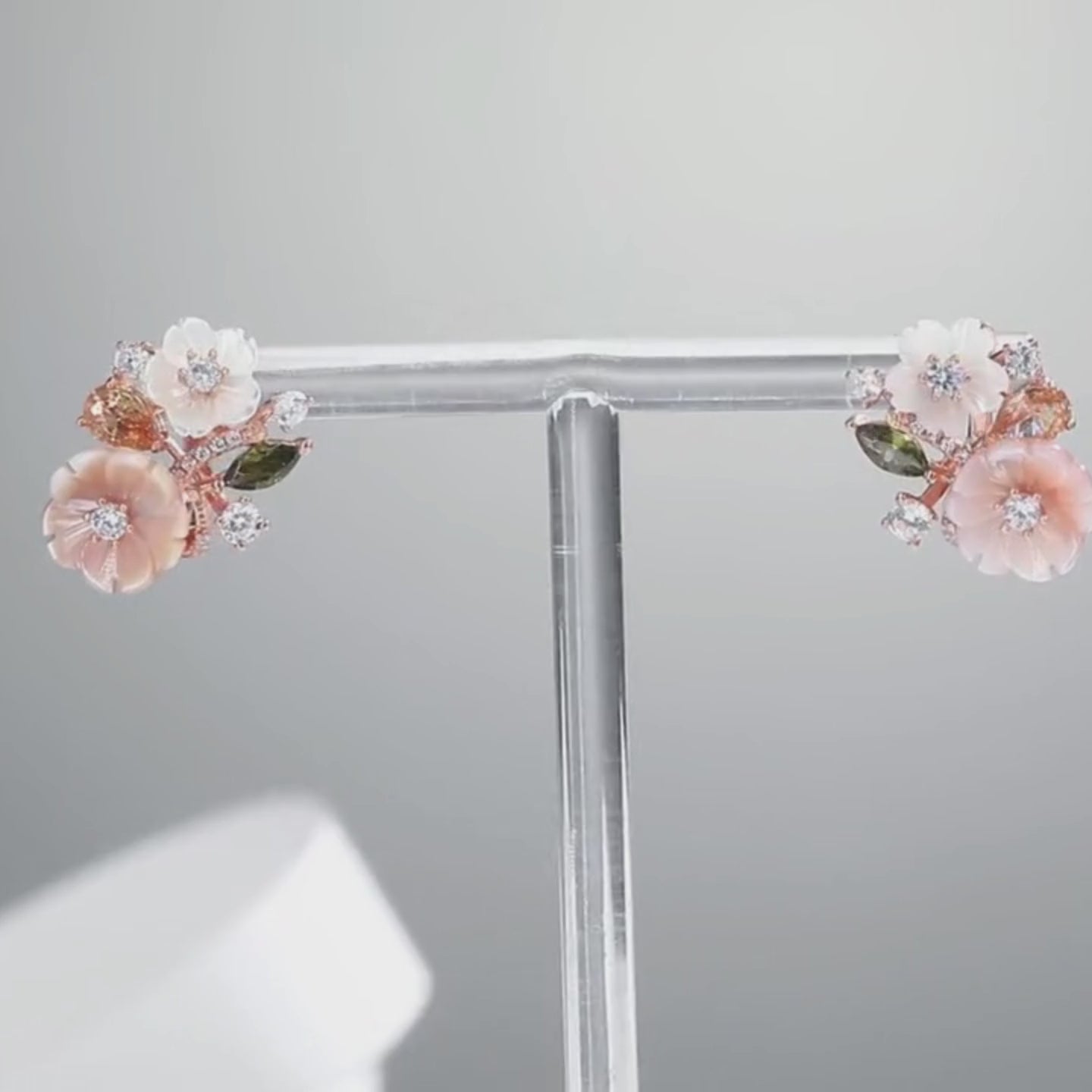 Begonia floral earrings with carved peach and ivory petals, accented by sparkling white and violet stones in a rose gold setting.

