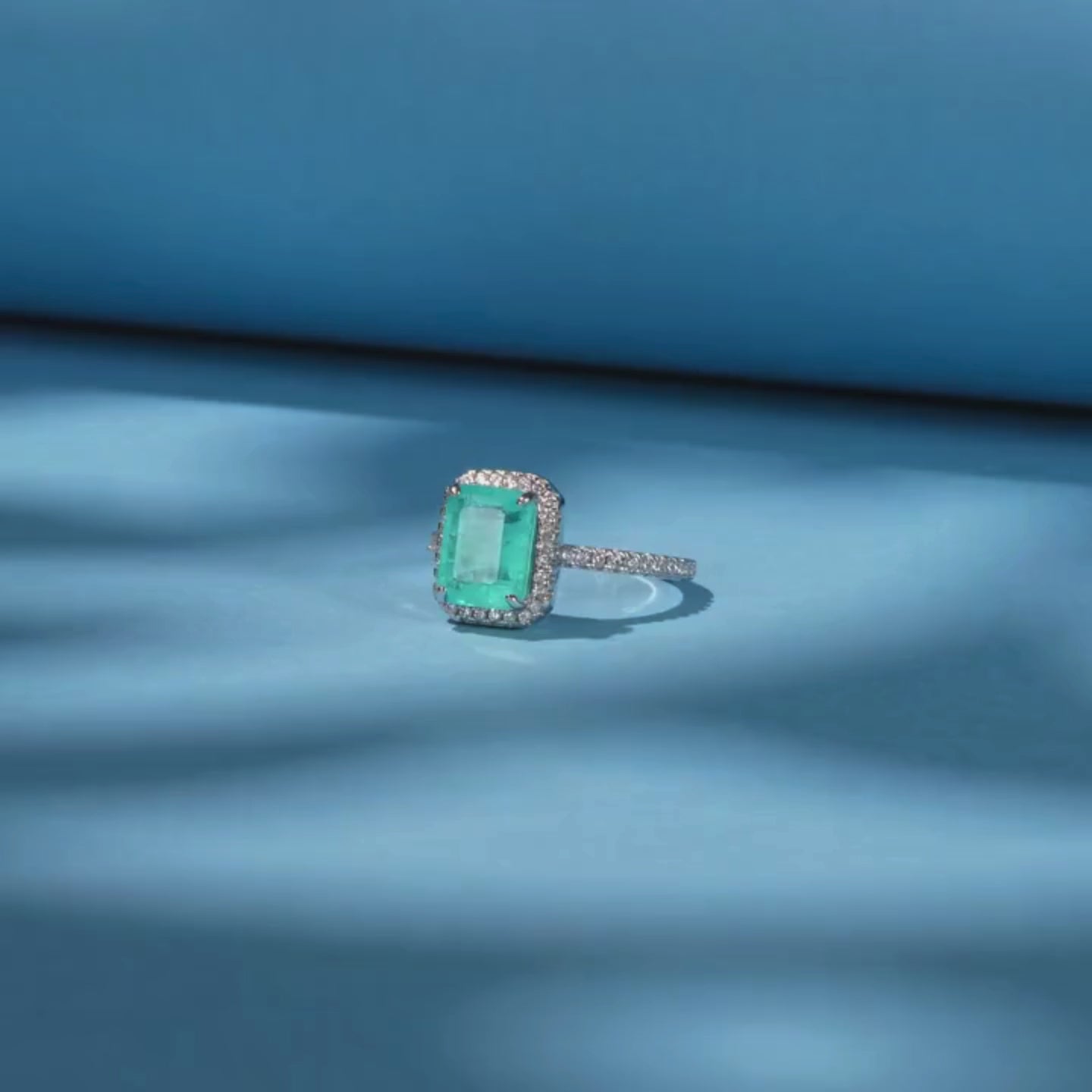 Rectangular green gemstone ring with a halo of clear stones on a silver band.

