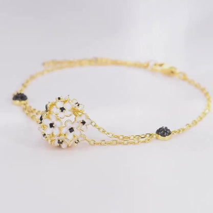Gold bracelet featuring a cluster of white enamel flowers with black stone centers, from the Fiore Scuro line.

