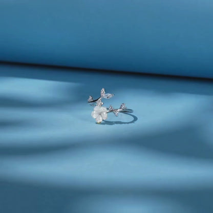 Delicate silver ring featuring a white carved flower and sparkling leaf-shaped stones arranged in a graceful, curved design.

