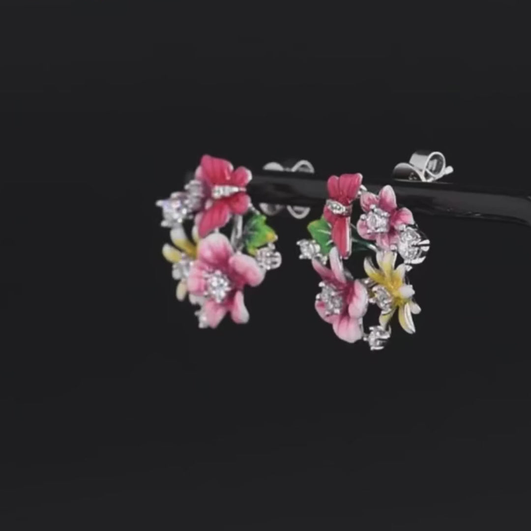 Pair of vibrant floral stud earrings with pink, red, and yellow enamel flowers accented by sparkling stones, set against a red background.

