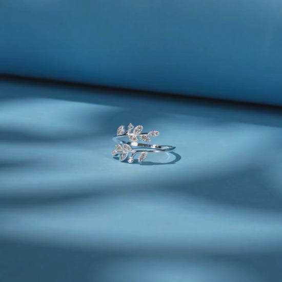 Silver ring designed with two curved branches, each adorned with pavé-set leaf shapes and tiny round white stones.

