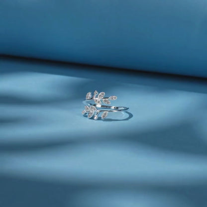 Silver ring designed with two curved branches, each adorned with pavé-set leaf shapes and tiny round white stones.

